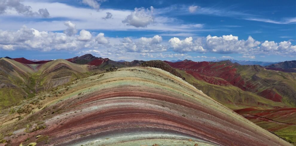 Vista panorámica de la Montaña Arcoíris de Palcoyo mostrando sus capas geológicas de colores bajo un cielo azul intenso
