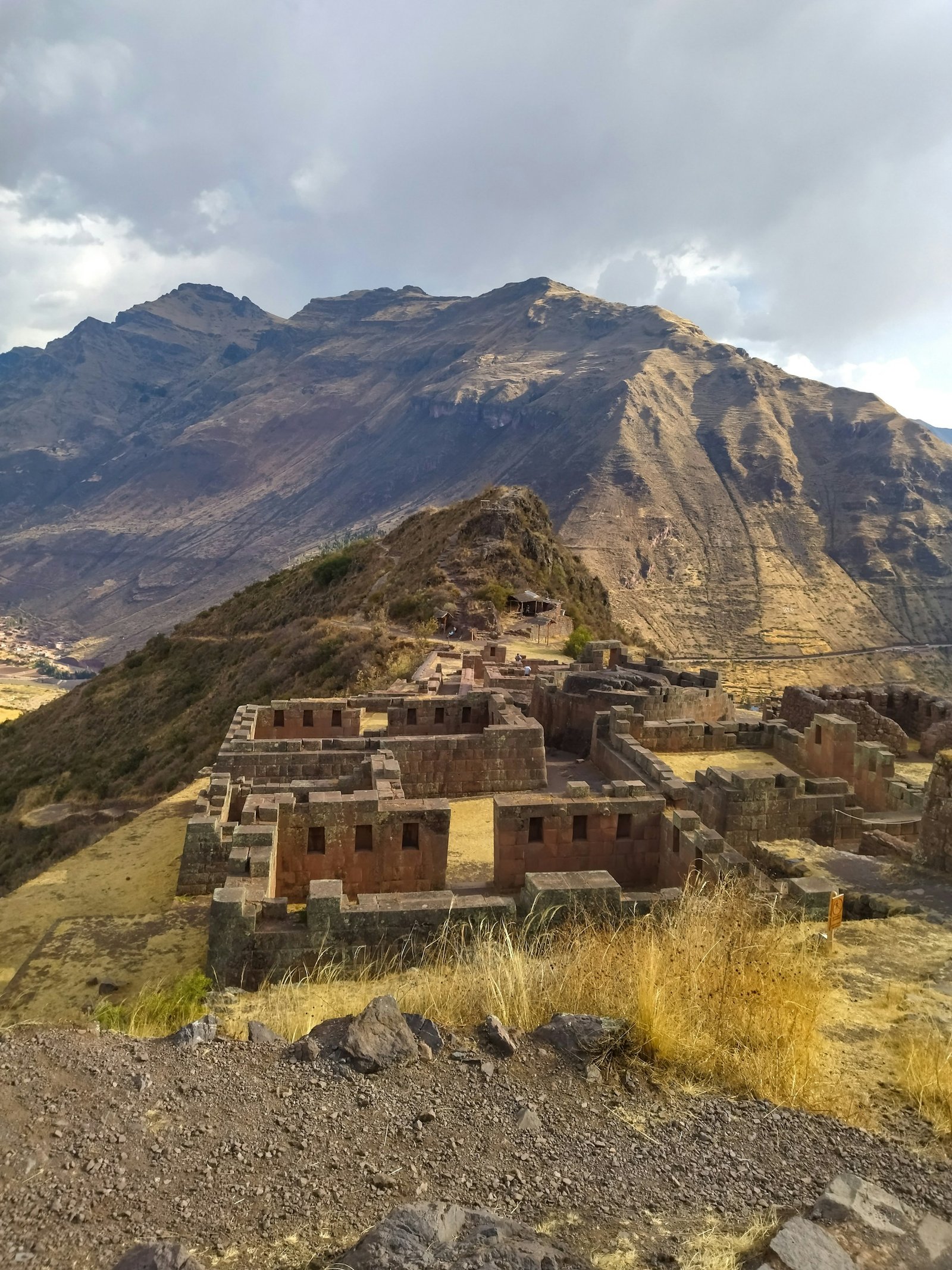 Ruinas incas de Pisac mostrando edificaciones de piedra en la cima de una montaña con impresionantes vistas panorámicas de los Andes cusqueños.
