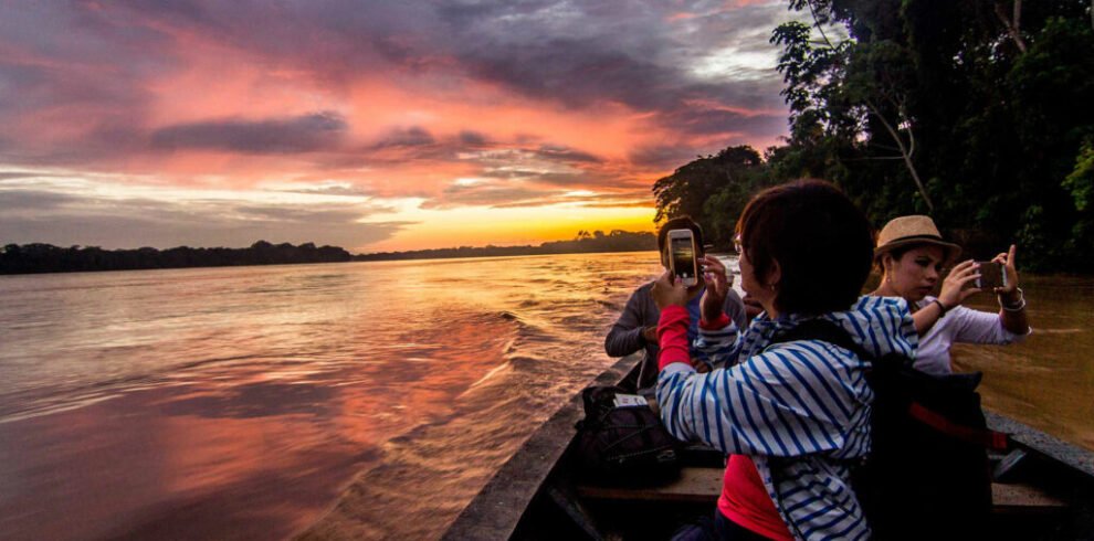 Turistas fotografiando atardecer amazónico desde embarcación en río de Puerto Maldonado
