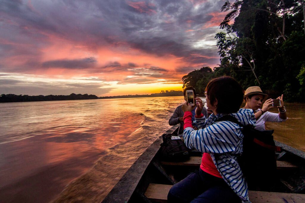 Turistas fotografiando atardecer amazónico desde embarcación en río de Puerto Maldonado