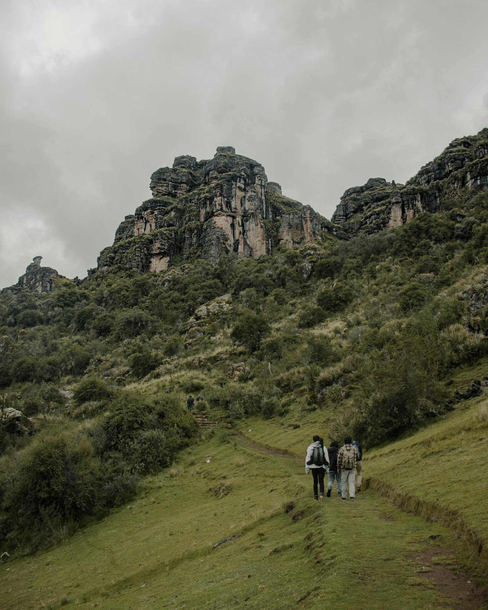 Trekking hacia Waqrapukara, viajeros caminando por sendero verde con formaciones rocosas al fondo