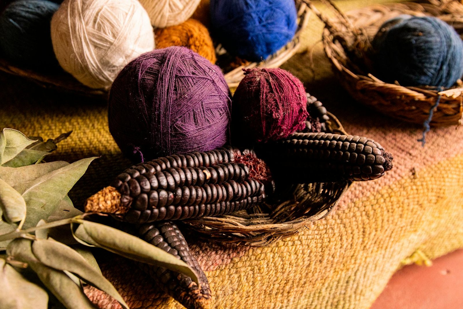 Madejas de lana teñida con tintes naturales en colores tradicionales junto a maíz morado andino