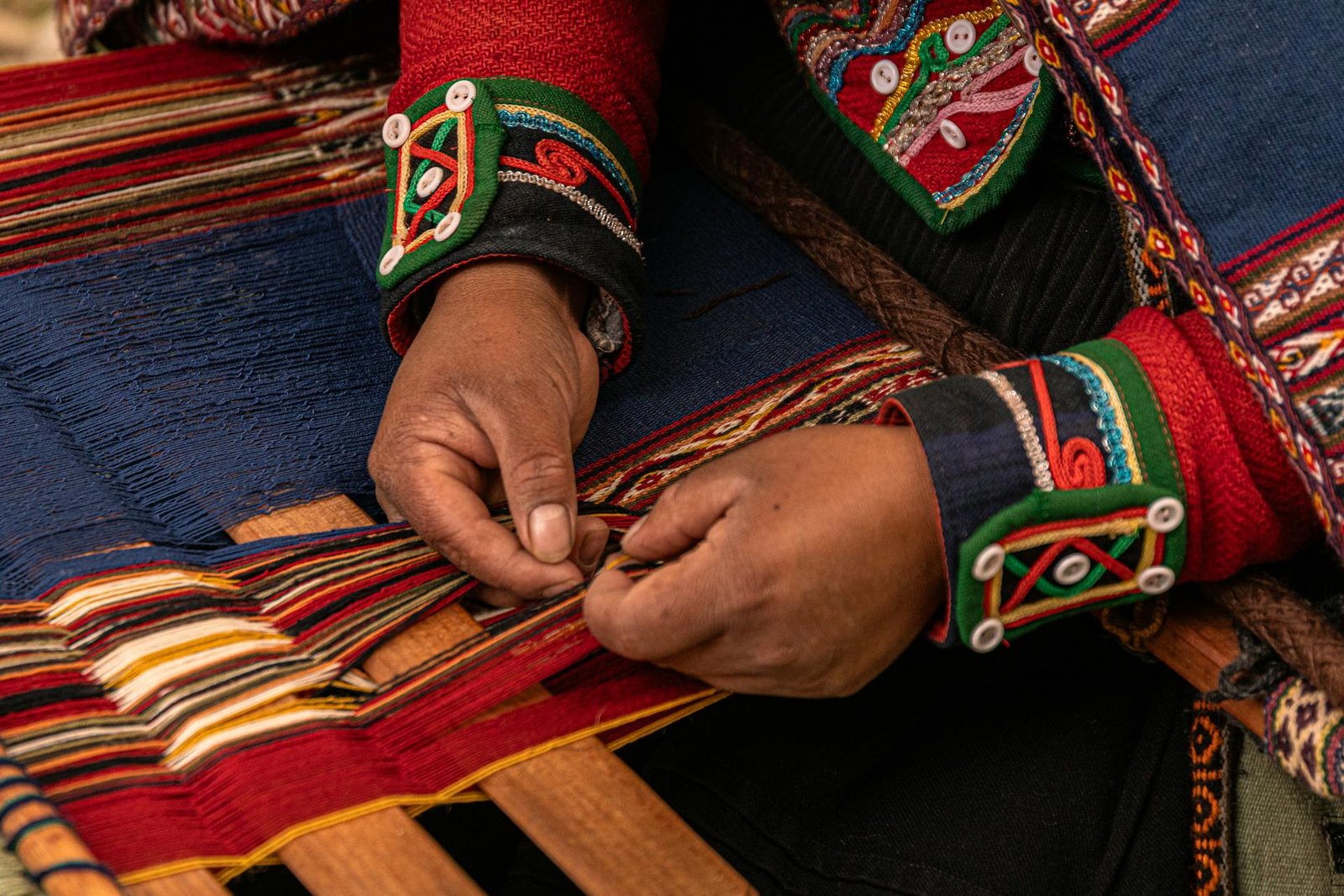Manos de tejedora andina trabajando en telar tradicional con textiles coloridos en Chinchero